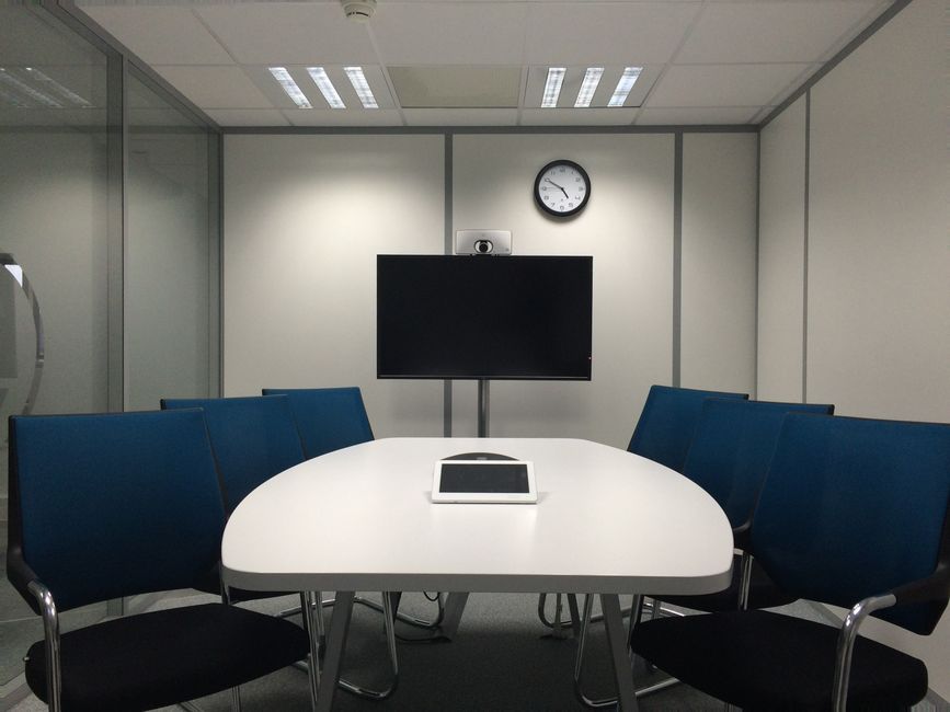 Employees gather around a conference table while a wall panel controls displays, lighting, and video conferencing equipment.